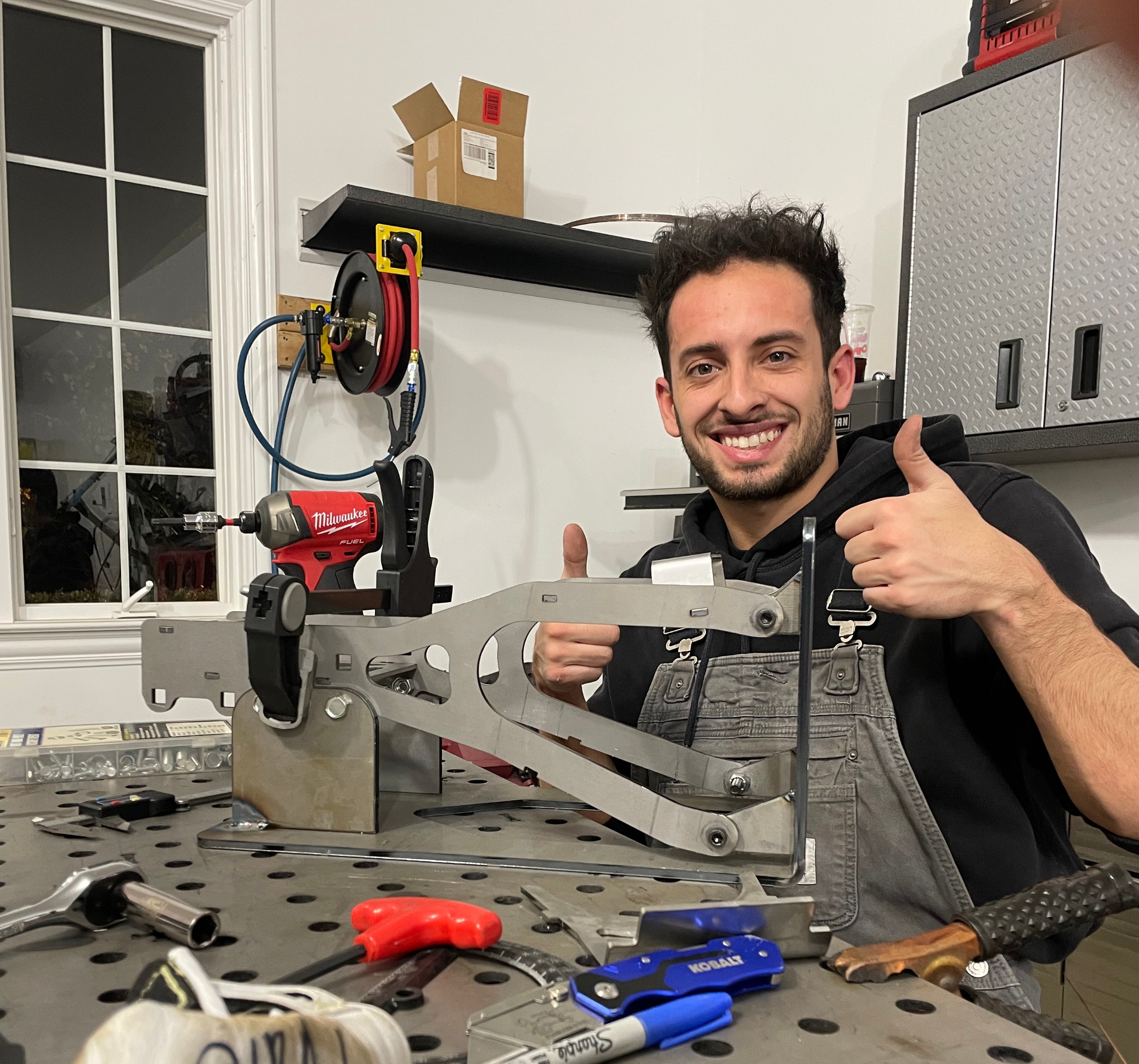 Nathan Arinta at the welding table, holding a custom fabricated bracket